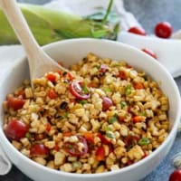 Bowl of grilled corn salad with tomatoes, bell pepper, and green onions in a white bowl.