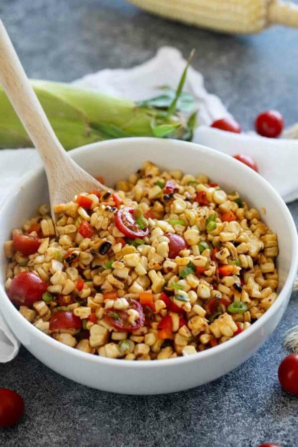 Bowl of grilled corn salad with tomatoes, bell pepper, and green onions in a white bowl.