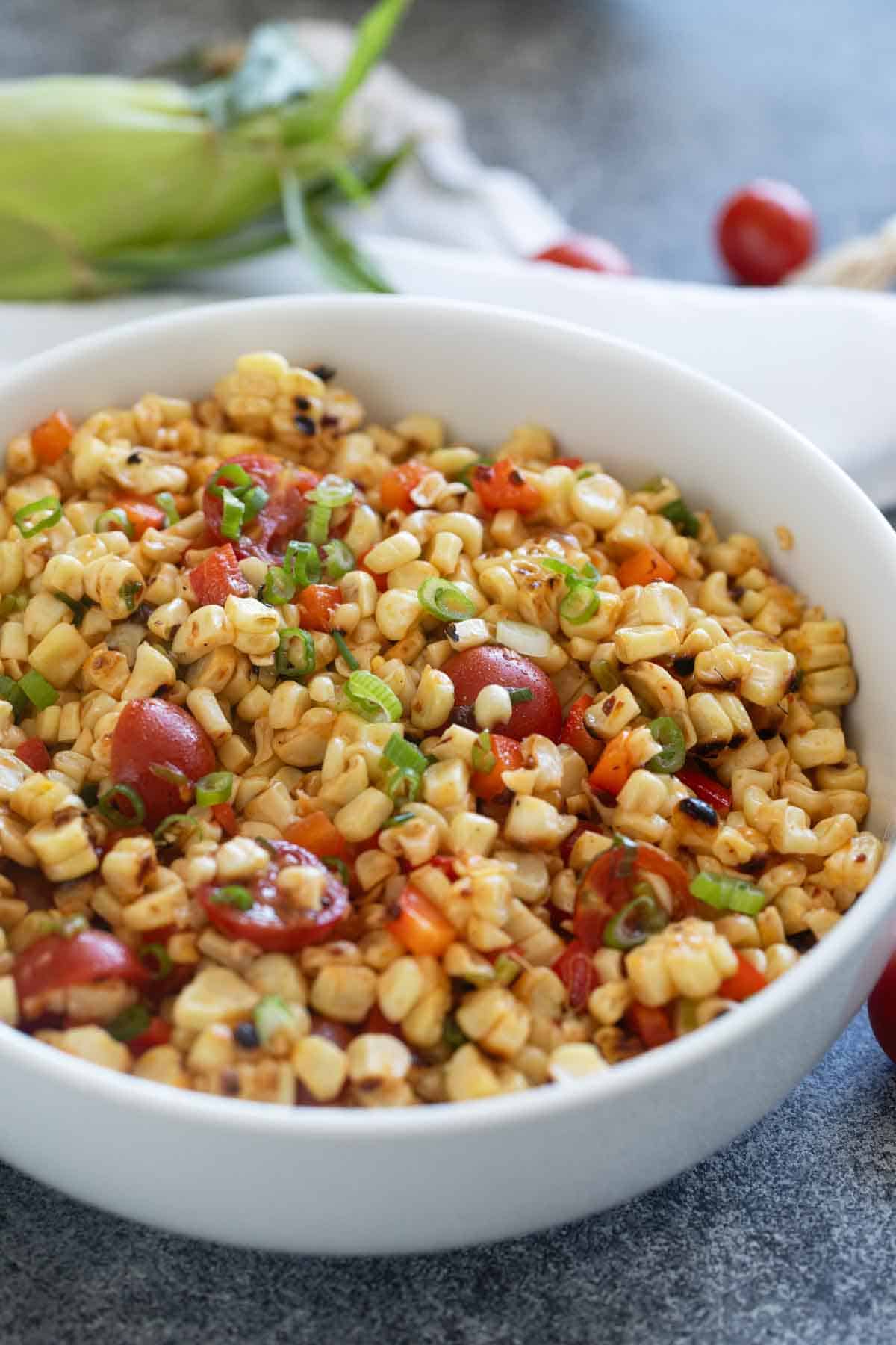 Bowl filled with grilled corn salad with tomatoes and green onions.