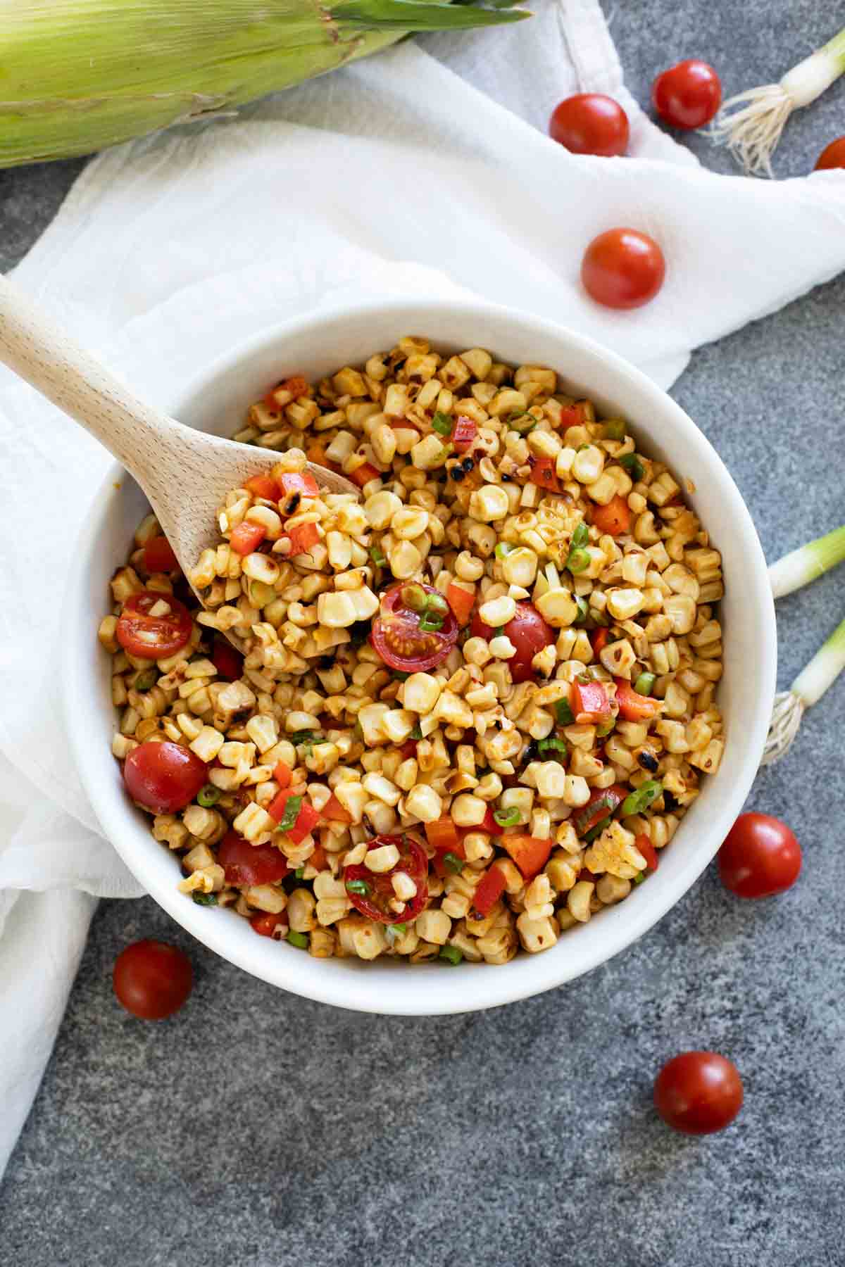 Bowl filled with Grilled Corn Salad with a wooden spoon.