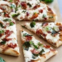Slices of Grilled White Pizza with Bacon and Basil with more fresh basil on the side.