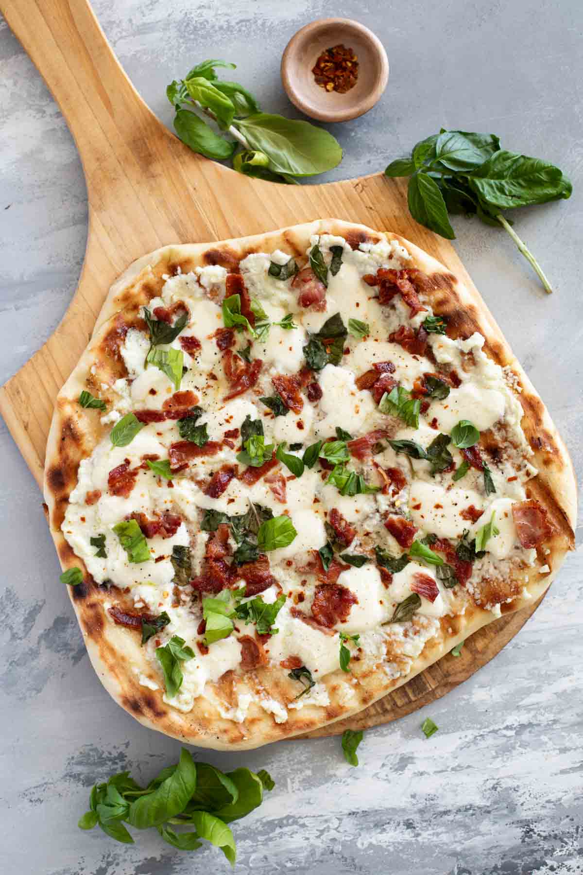 Full Grilled White Pizza with Bacon and Basil on a pizza peel.