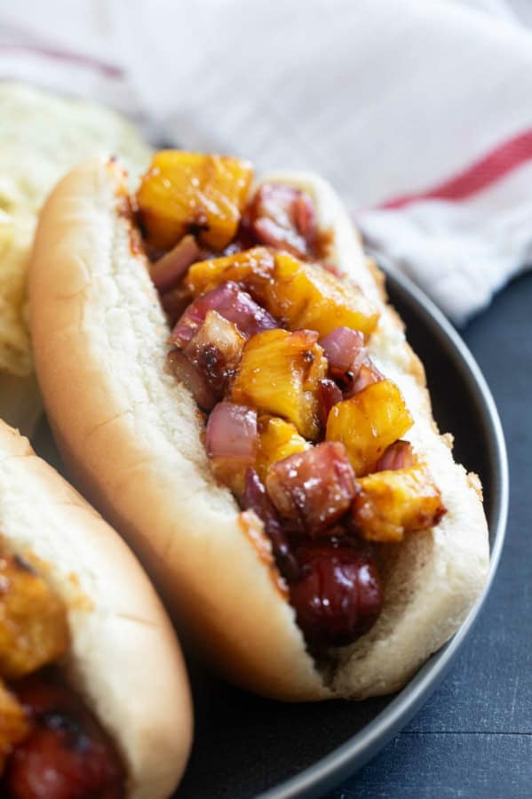 Hawaiian Hot Dogs with grilled pineapple and red onion with barbecue sauce.