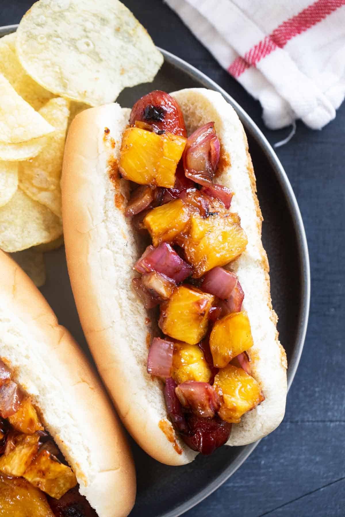 Hawaiian Hot Dogs on a plate topped with pineapple and onion.