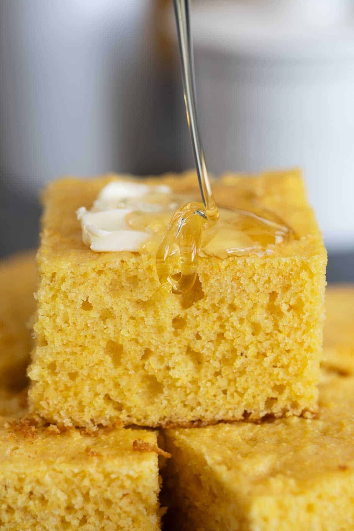Honey being drizzled on a slice of Sour Cream Cornbread.