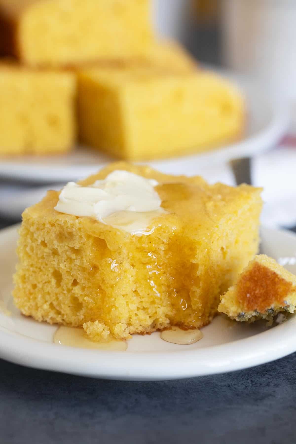 Slice of sour cream cornbread with butter and honey and a bite taken from it.
