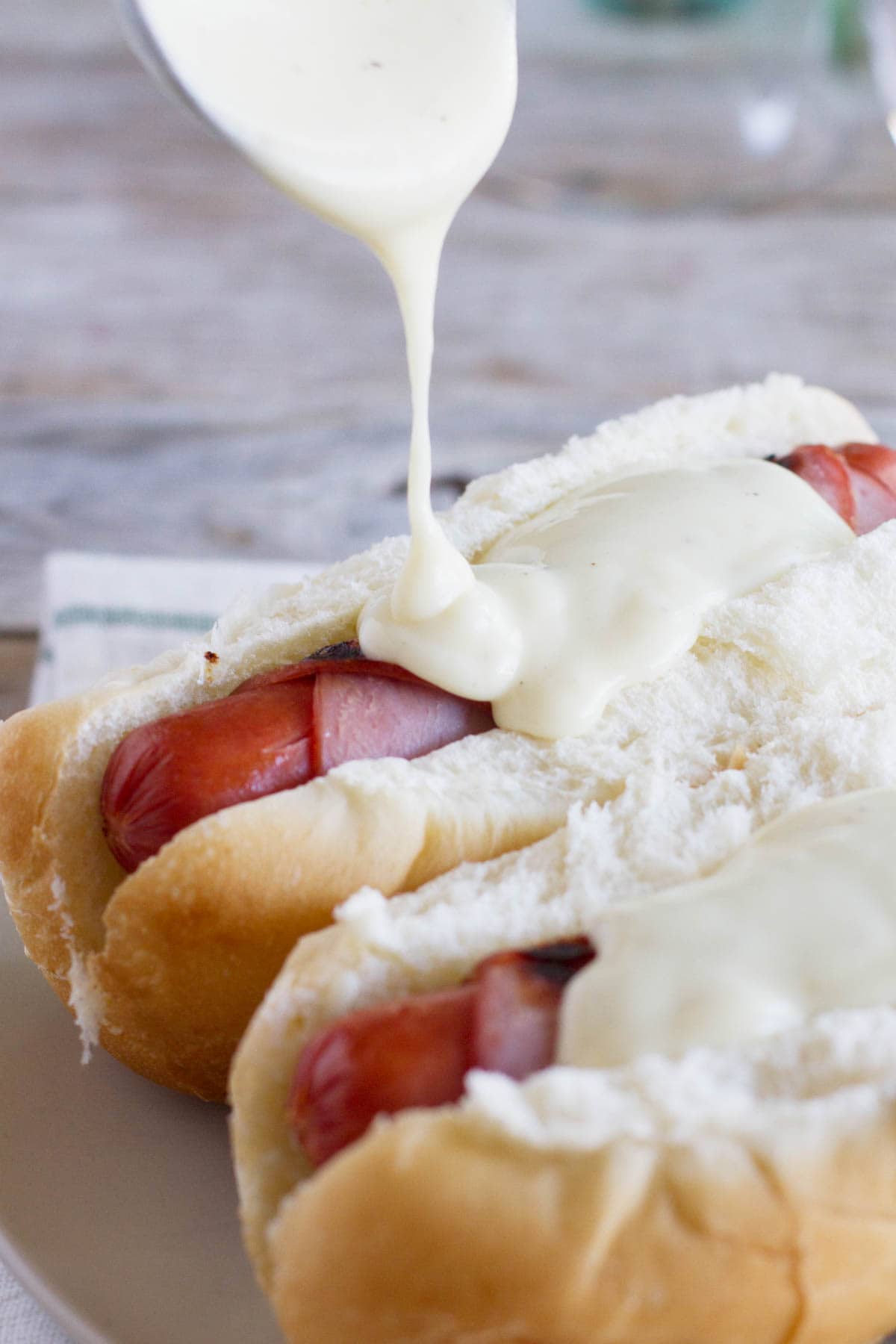 pouring cheese sauce on Cordon Bleu Hot Dogs.