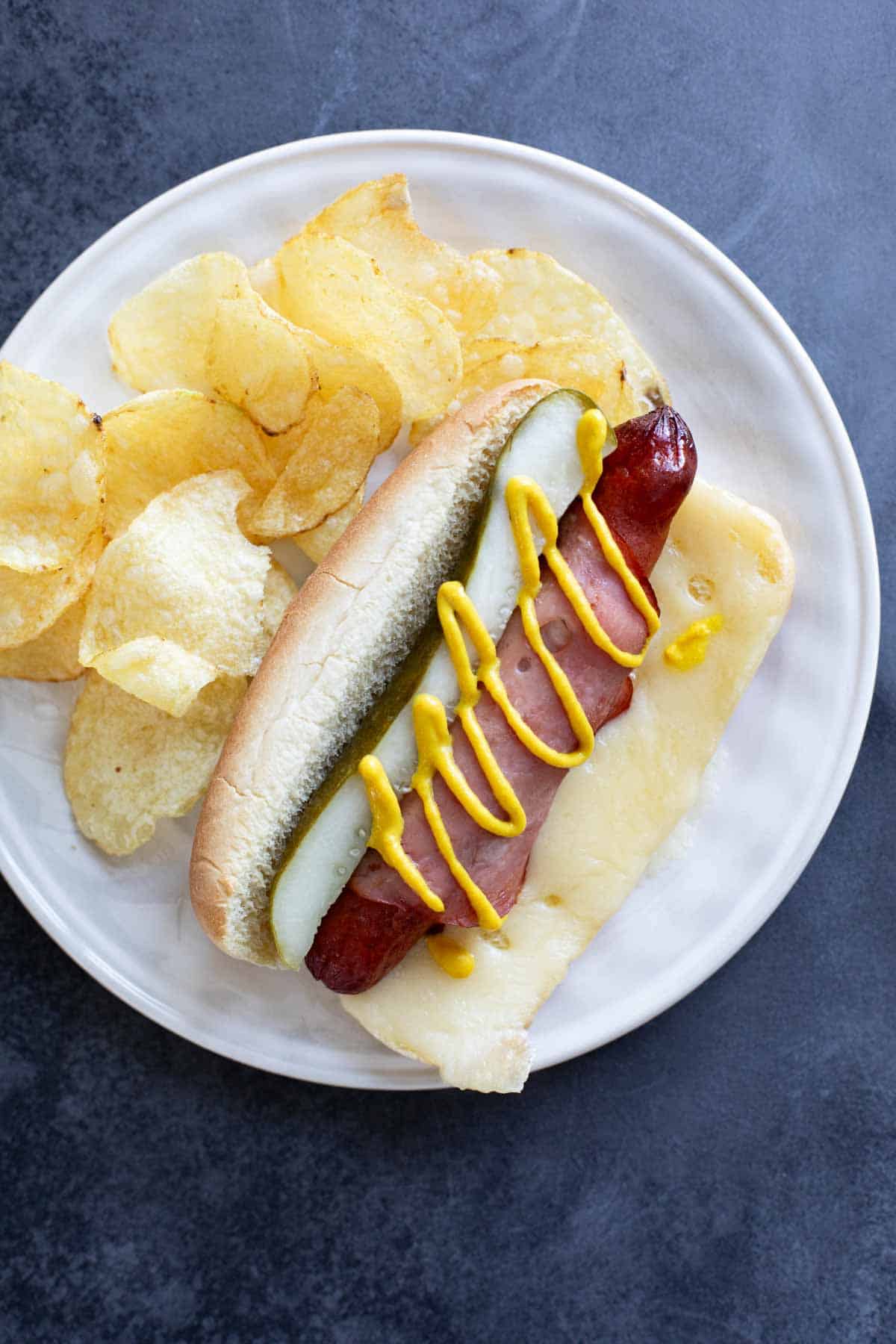 Cuban hot dog on a plate with potato chips.