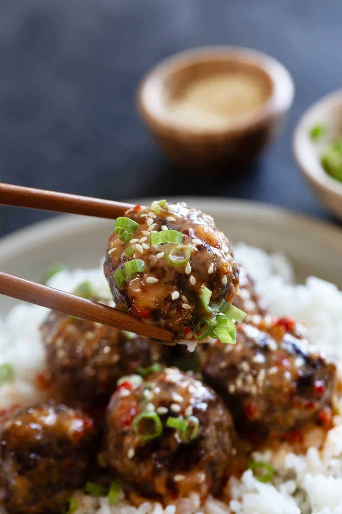 Firecracker Meatballs on a plate with one meatball being held by chopsticks.