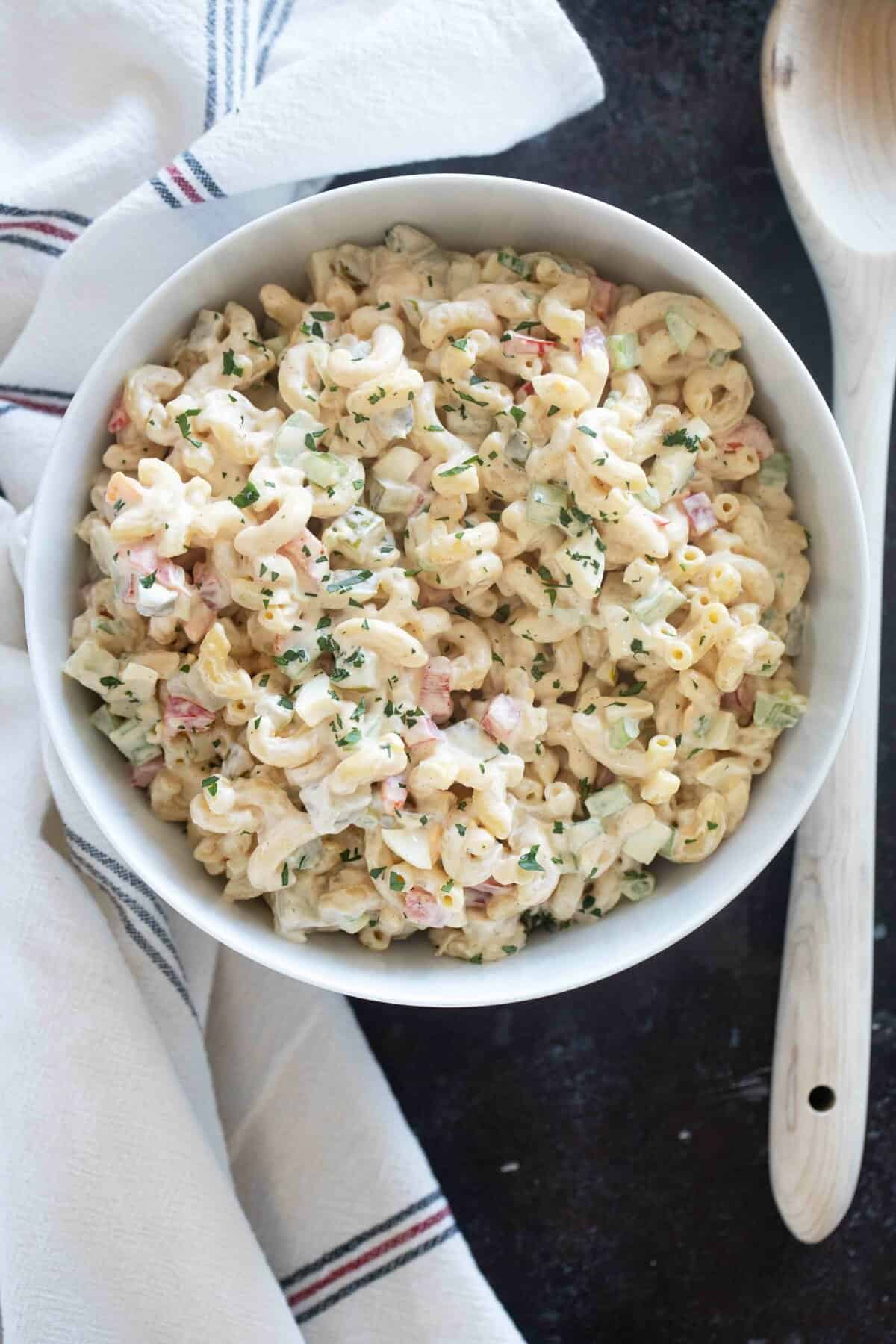 Bowl filled with macaroni salad with a kitchen towel and a wooden serving spoon.