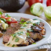 Plate with Mexican Spiced Steaks with Chile Con Queso with tomato and avocado salad on the side.