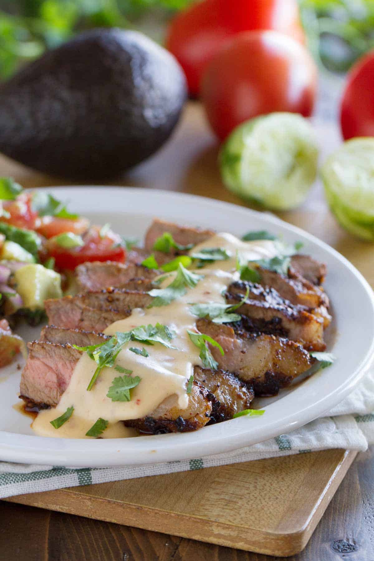 Plate with Mexican Spiced Steaks with Chile Con Queso with tomato and avocado salad on the side.