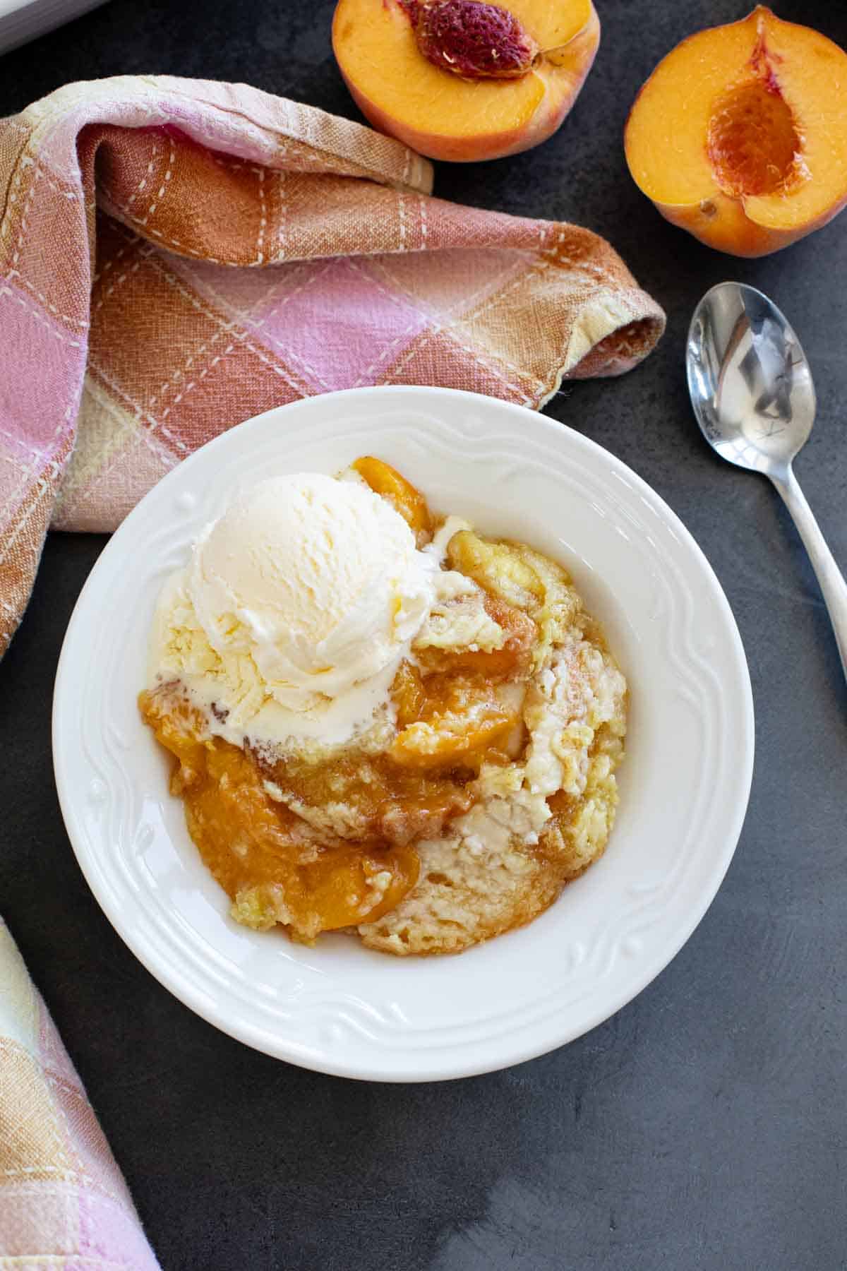 Bowl of peach dump cake with a scoop of vanilla ice cream on top.