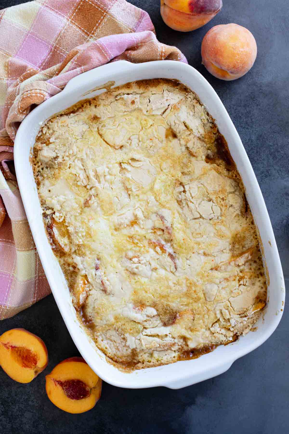 Baking dish with peach dump cake, with fresh peaches on the side.