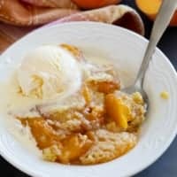 Bowl of peach dump cake topped with ice cream.