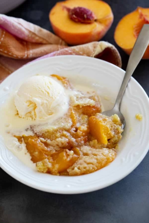 Bowl of peach dump cake topped with ice cream.