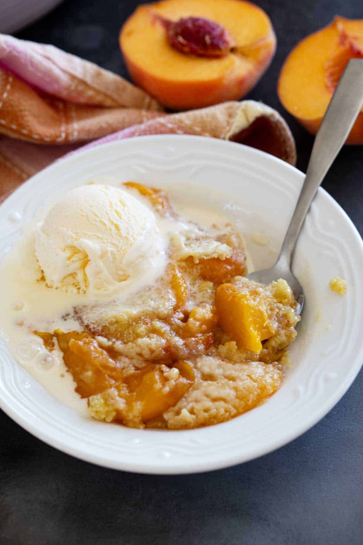 Bowl of peach dump cake topped with ice cream.