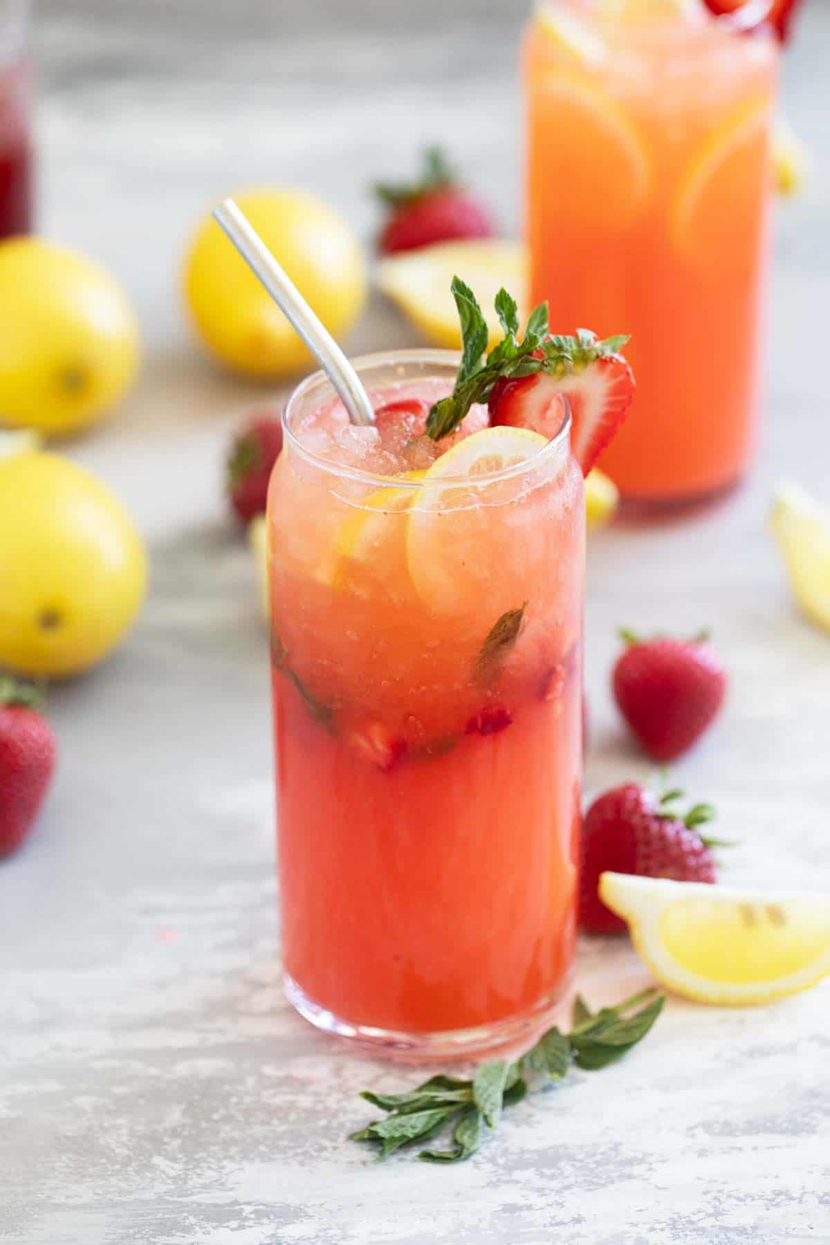 Glass of strawberry lemonade with fresh strawberry chunks and mint, served with a metal straw.