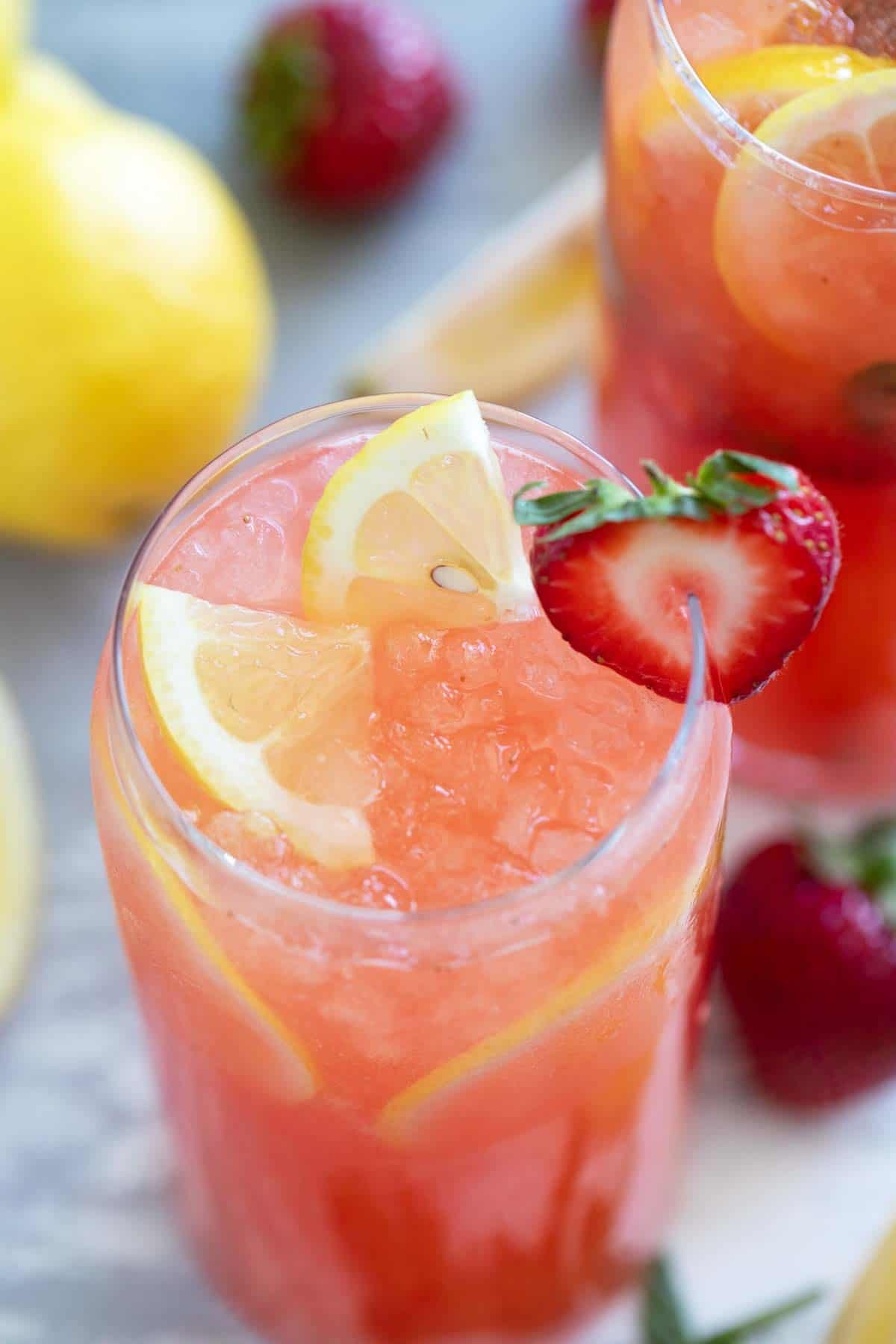 Glass of strawberry lemonade, topped with lemon slices and a fresh strawberry slice.
