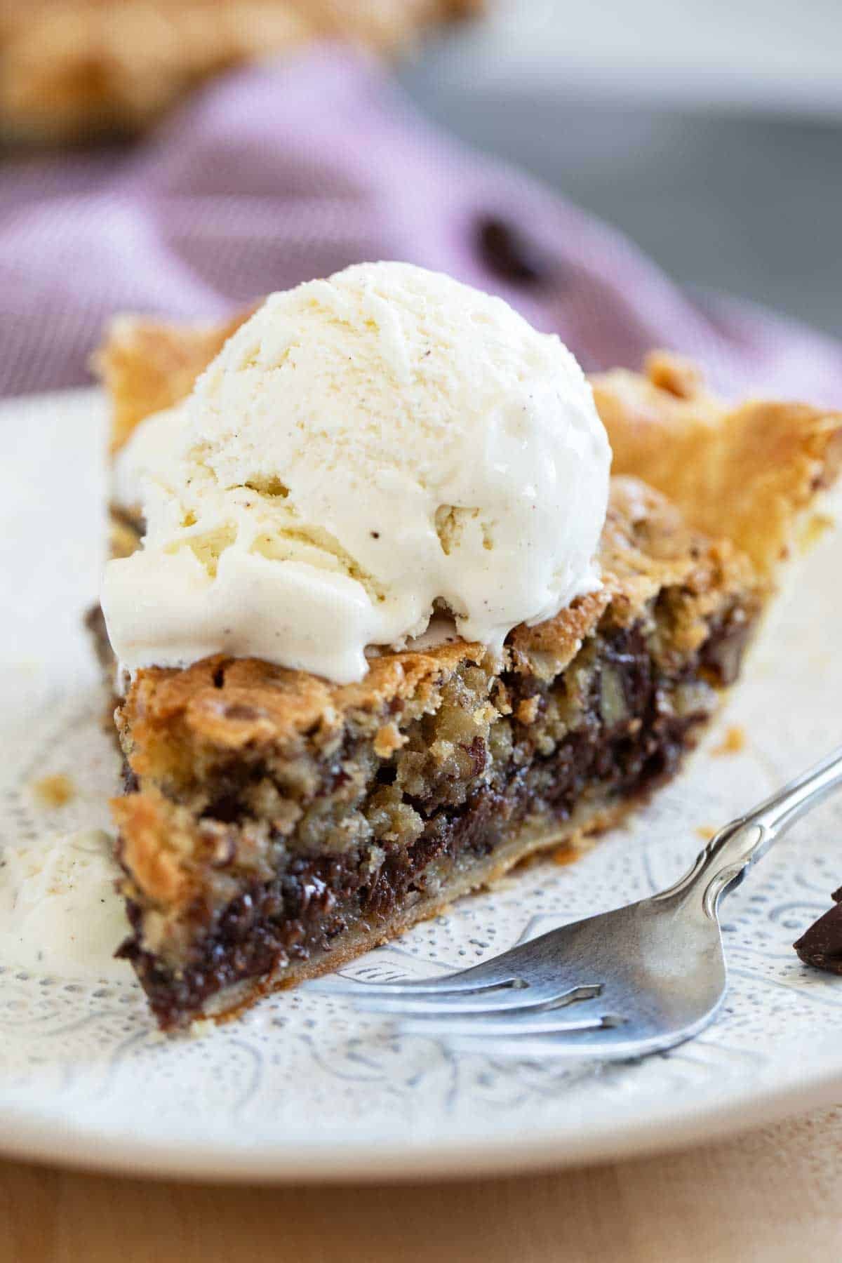 Slice of warm chocolate chip cookie pie with ice cream and a fork.