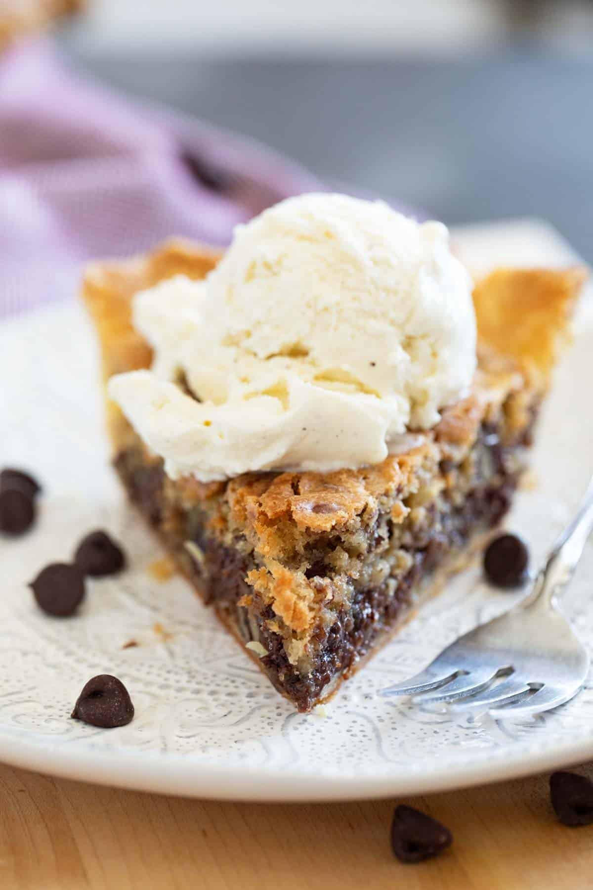 Slice of chocolate chip cookie pie, topped with a scoop of vanilla ice cream.