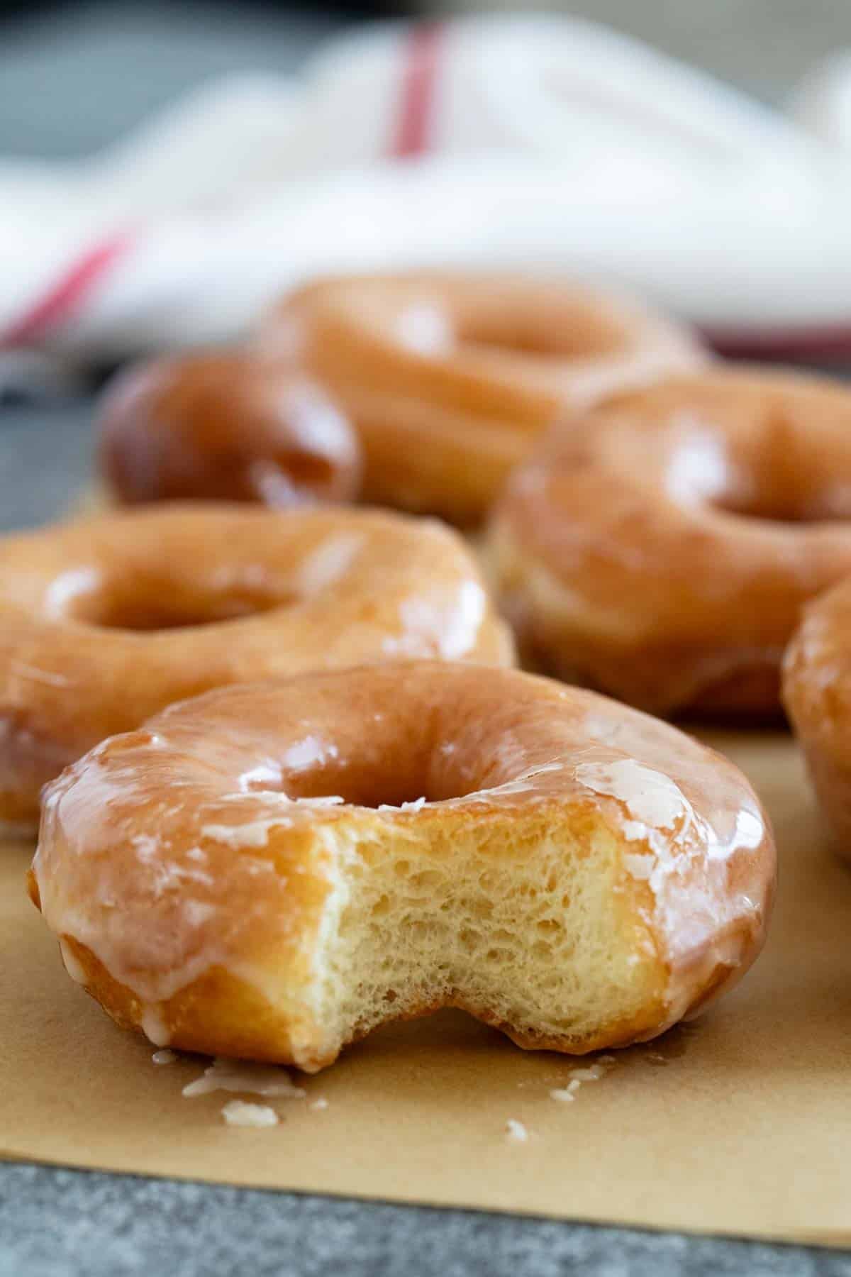 Homemade glazed donuts with a bite taken from one of them.