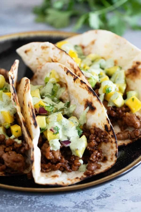 Plate with 3 Hawaiian Tacos topped with pineapple mango salsa and cilantro lime sauce.