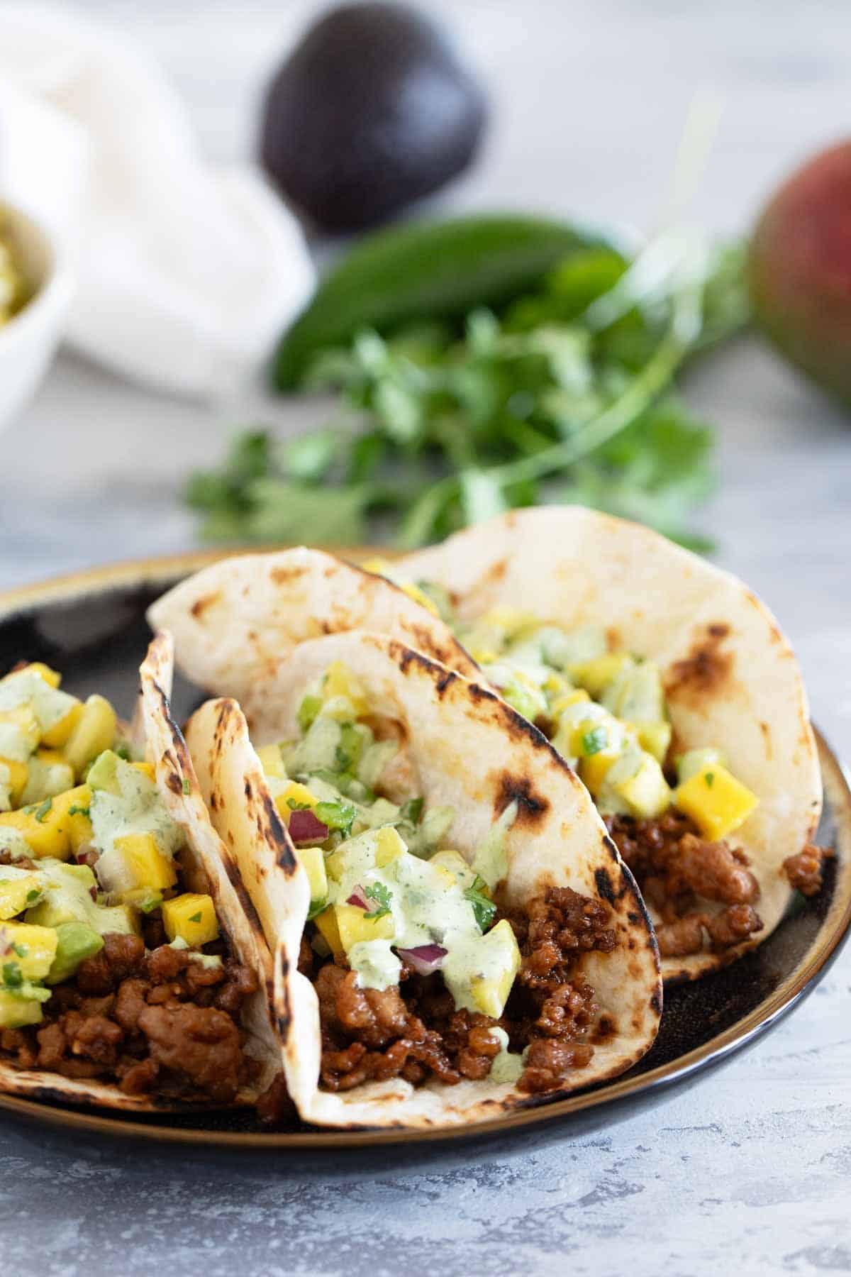 Hawaiian Tacos on a plate, topped with fruit salsa and cilantro lime sauce.