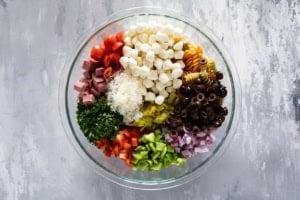Adding Italian pasta salad ingredients to a bowl.