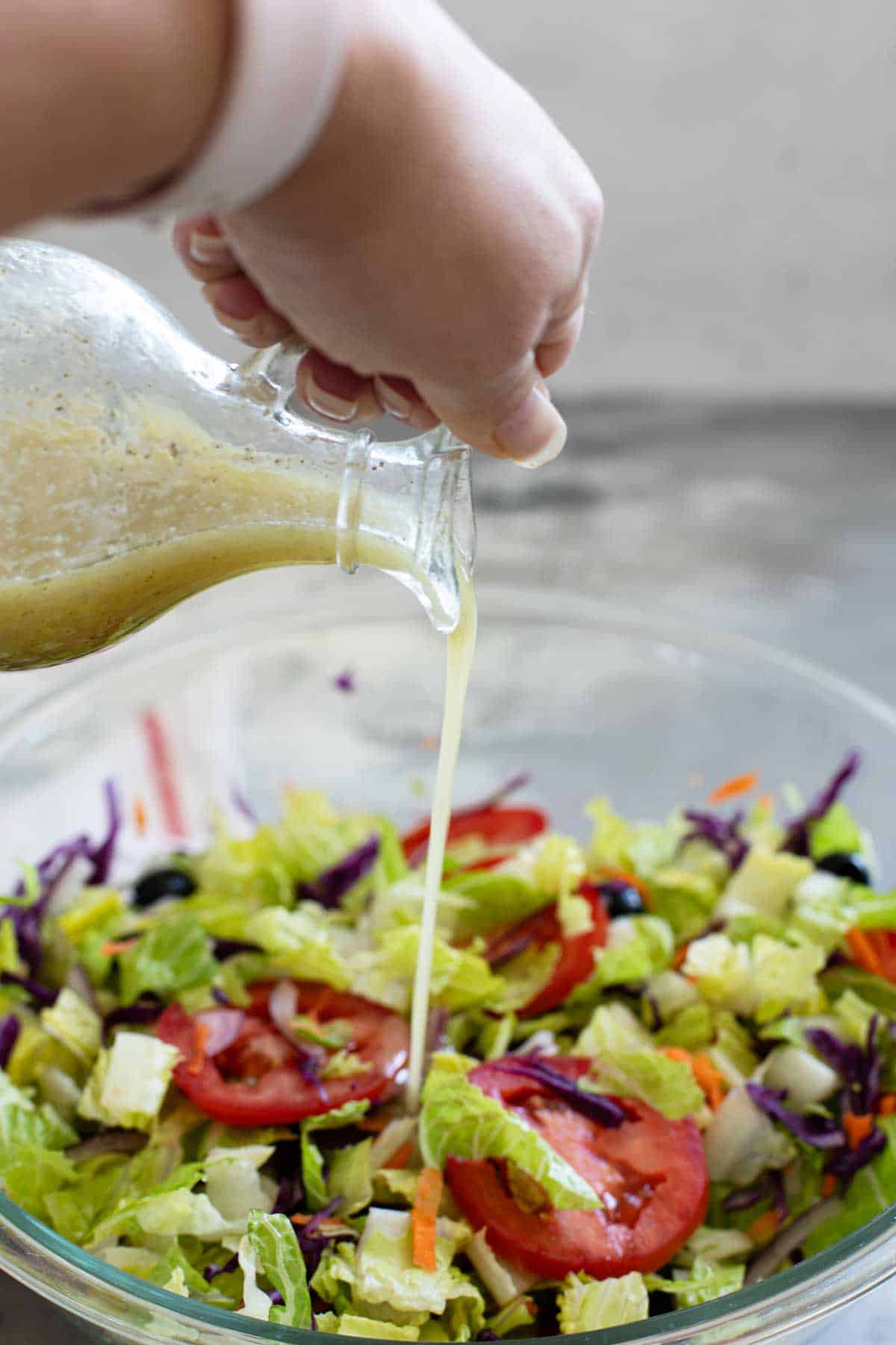 Pouring Olive Garden Salad Dressing over a salad.