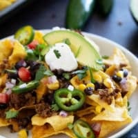 Sheet Pan Nachos on a plate, topped with sour cream, cilantro, and jalapeños.