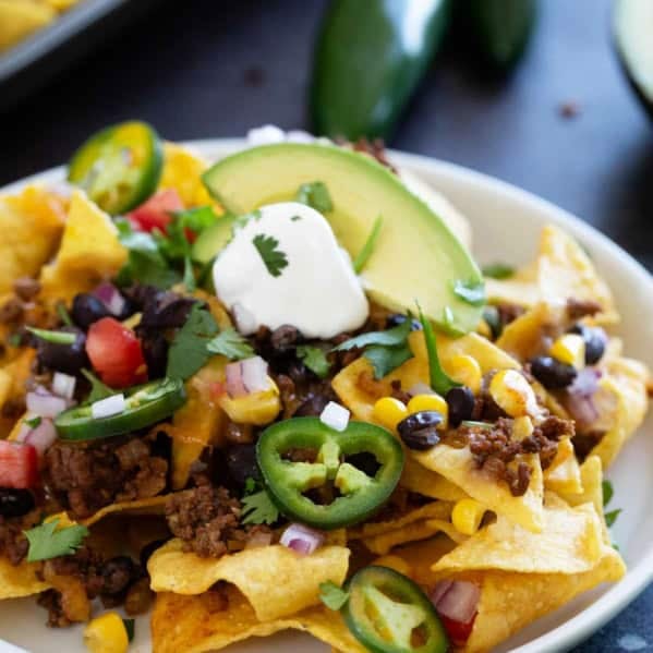 Sheet Pan Nachos on a plate, topped with sour cream, cilantro, and jalapeños.