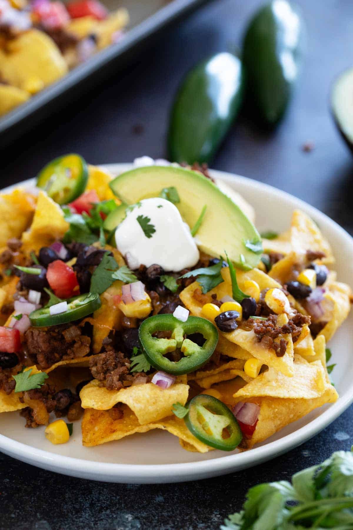 Sheet Pan Nachos on a plate, topped with sour cream, cilantro, and jalapeños.