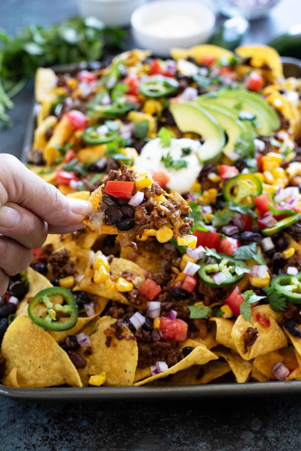 Holding a chip from a pan of Sheet Pan Nachos.