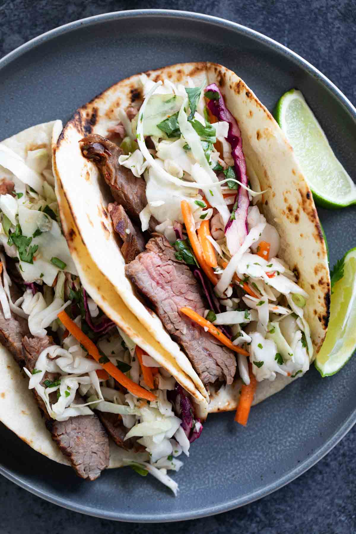 Two Thai Tacos on a plate, topped with cilantro lime slaw.