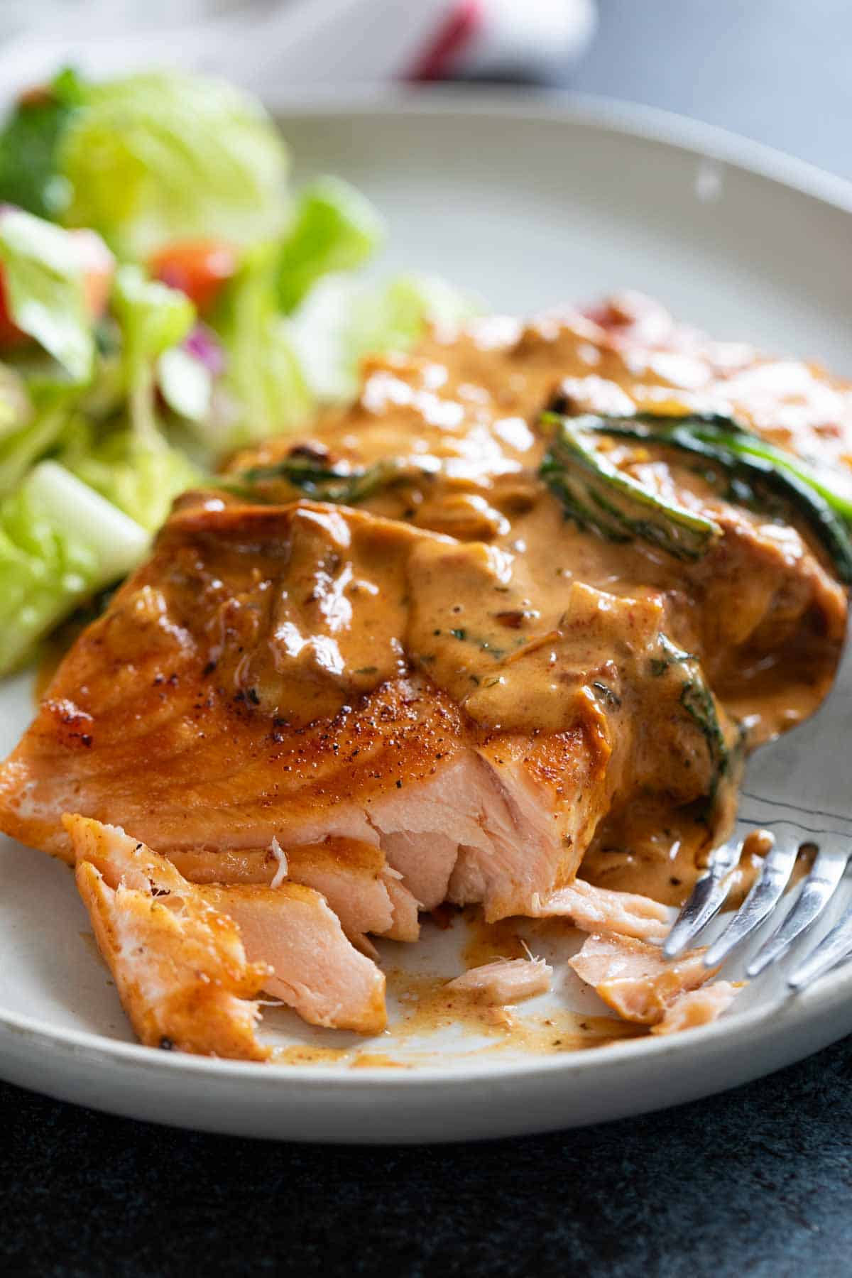 Serving of Tuscan Salmon on a plate with a bite taken from it.
