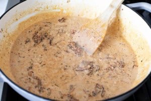 Adding cream and cheese to sun-dried tomatoes for salmon sauce.