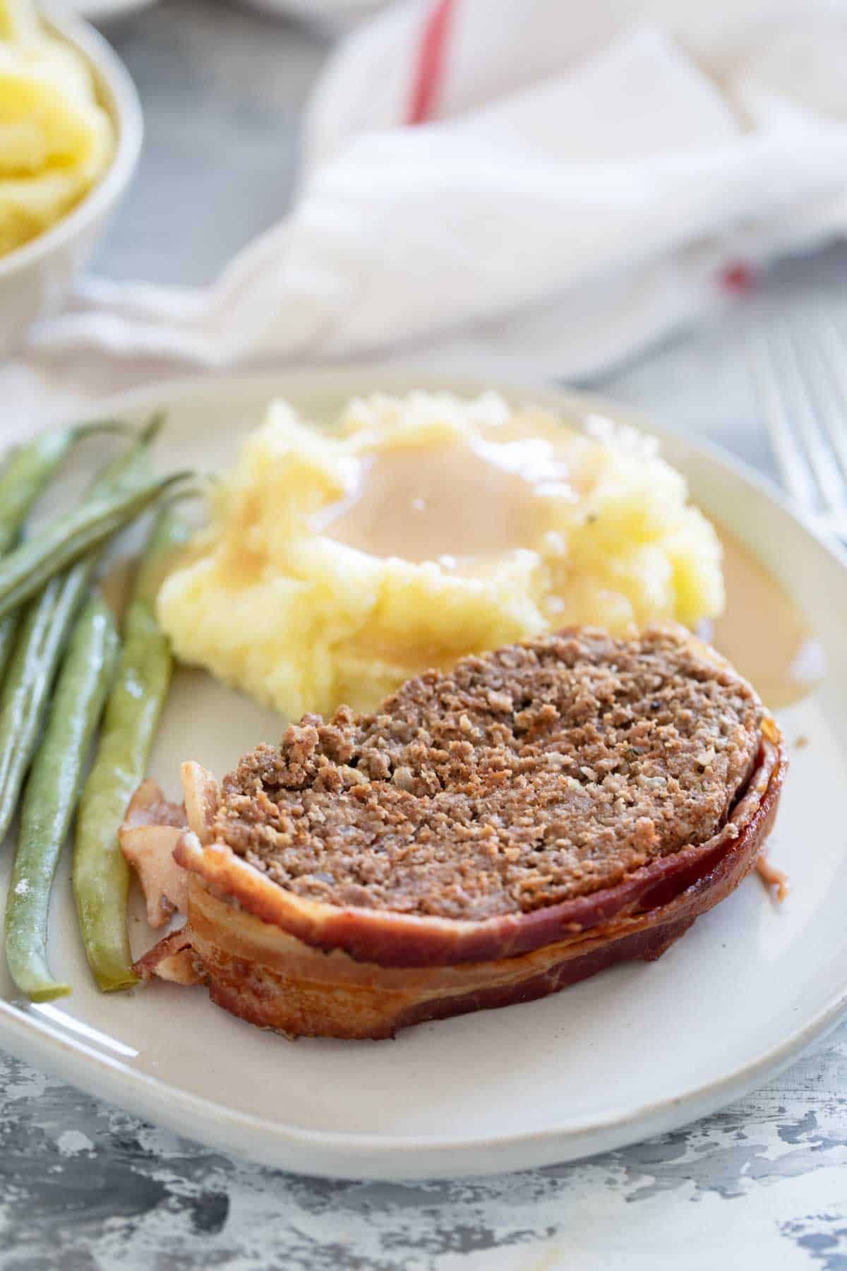 Serving of Bacon Wrapped Meatloaf with sides on a plate.