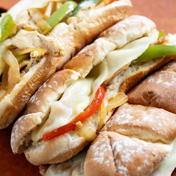 Three Chicken Cheesesteak Sandwiches on a cutting board.