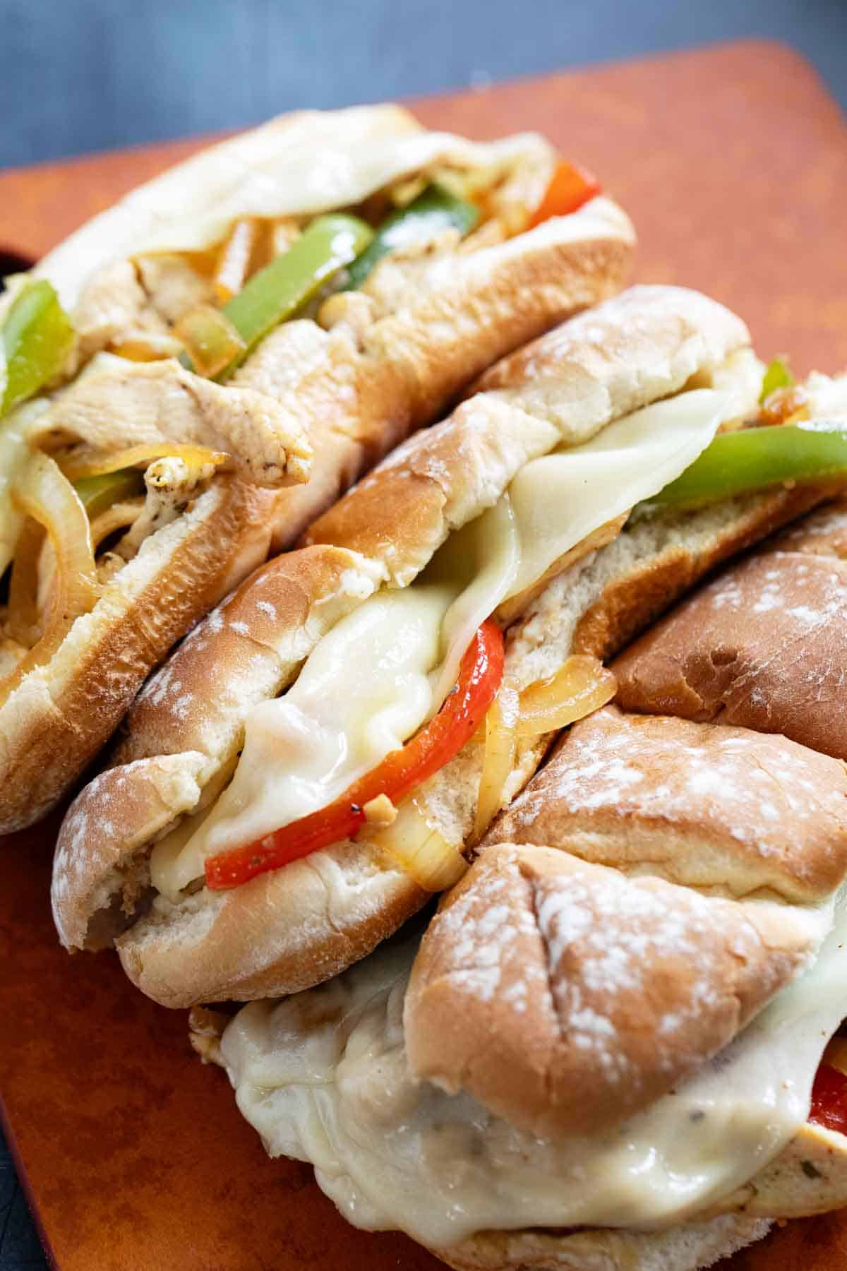 Three Chicken Cheesesteak Sandwiches on a cutting board.