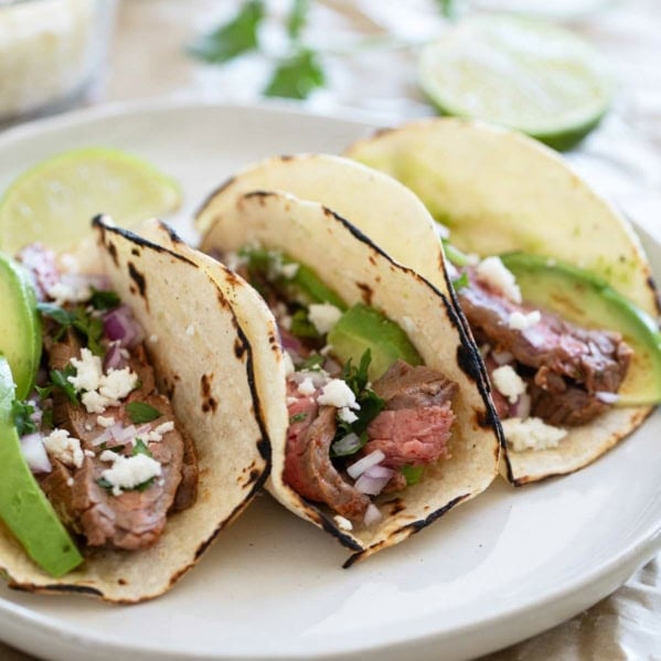 Flank Steak Tacos on corn tortillas on a plate.