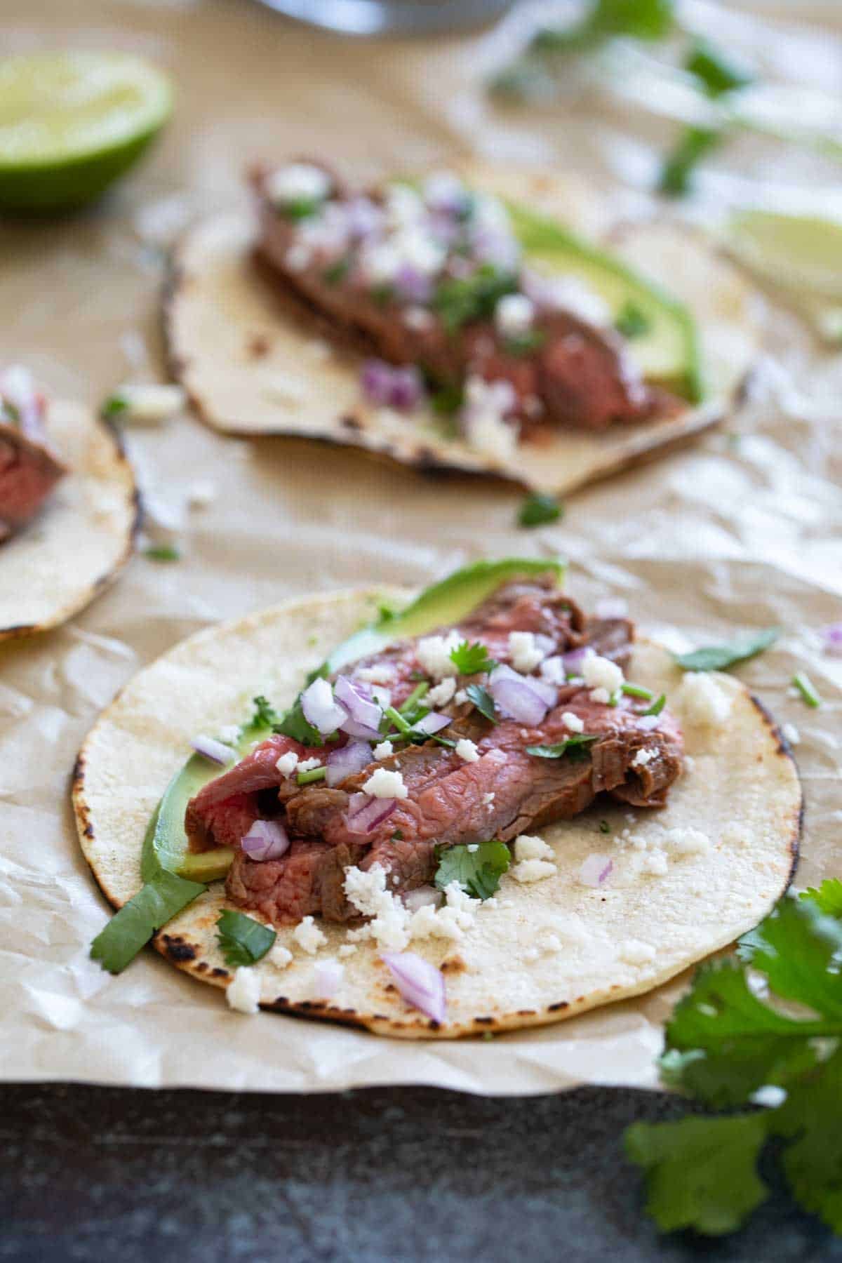 Flank Steak Tacos with avocado, cilantro, onions, and queso fresco.