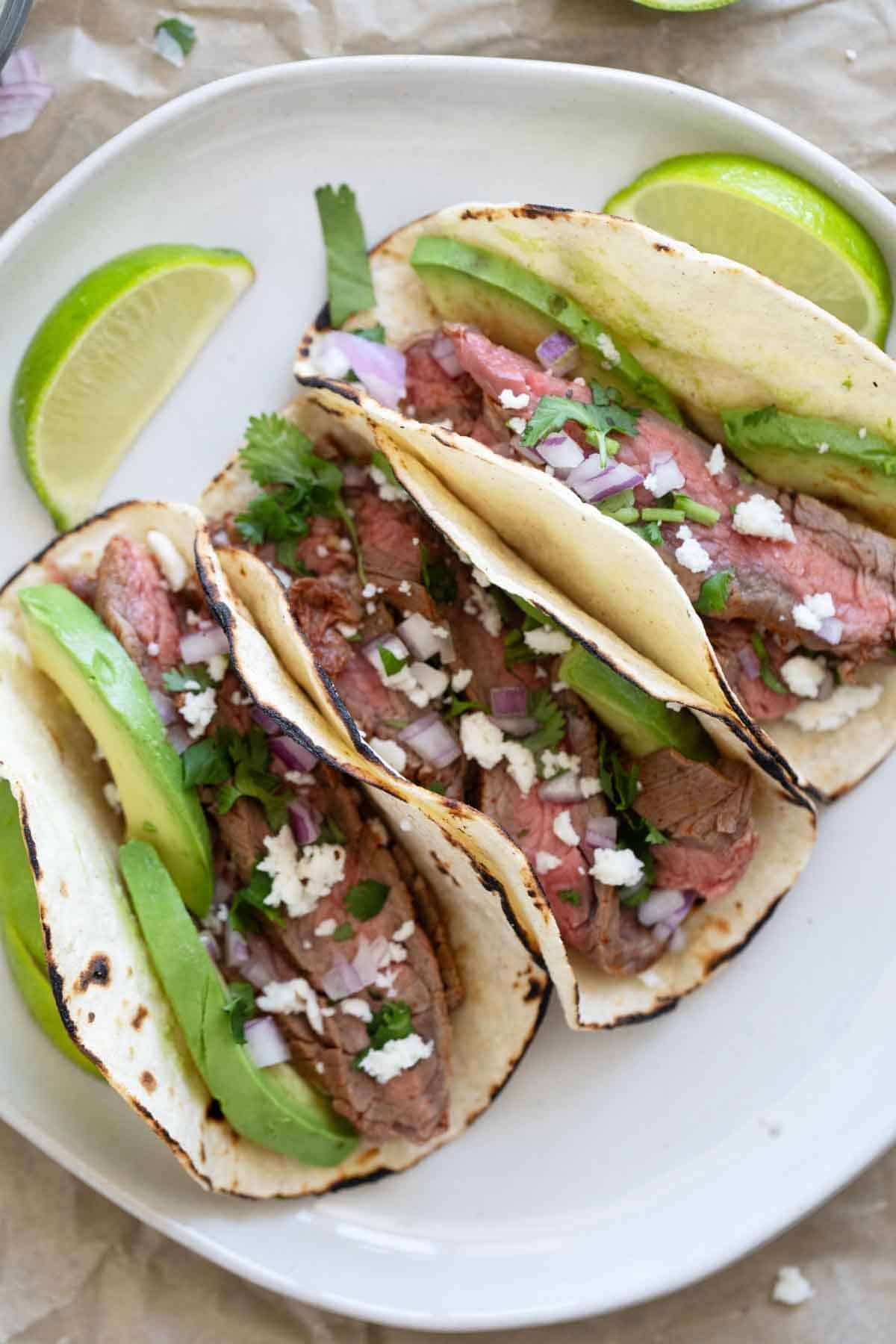 Three flank steak tacos on a plate.