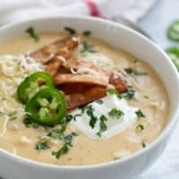 Bowl of Green Chicken Enchilada Soup topped with sour cream, cheese, tortilla strips, cilantro, and jalapeños.