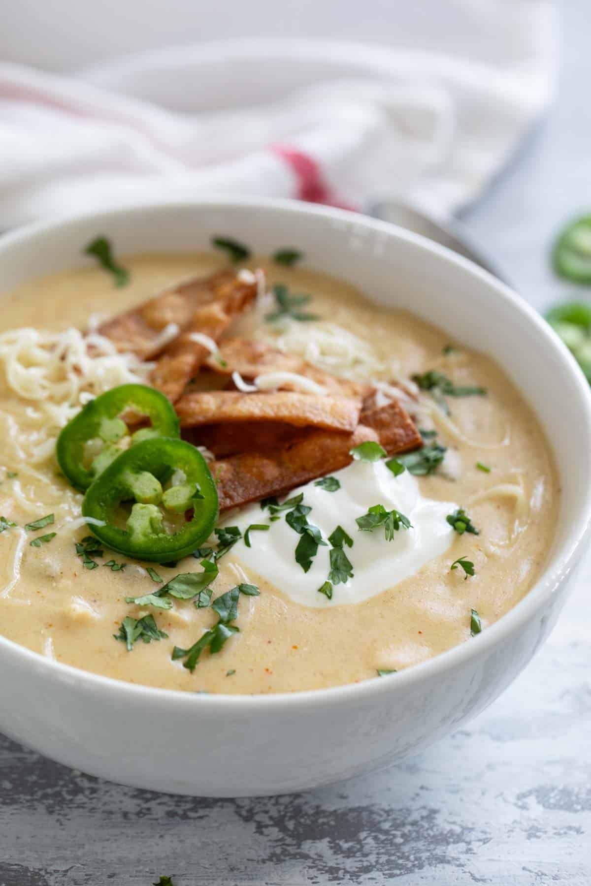 Bowl of Green Chicken Enchilada Soup topped with sour cream, cheese, tortilla strips, cilantro, and jalapeños.