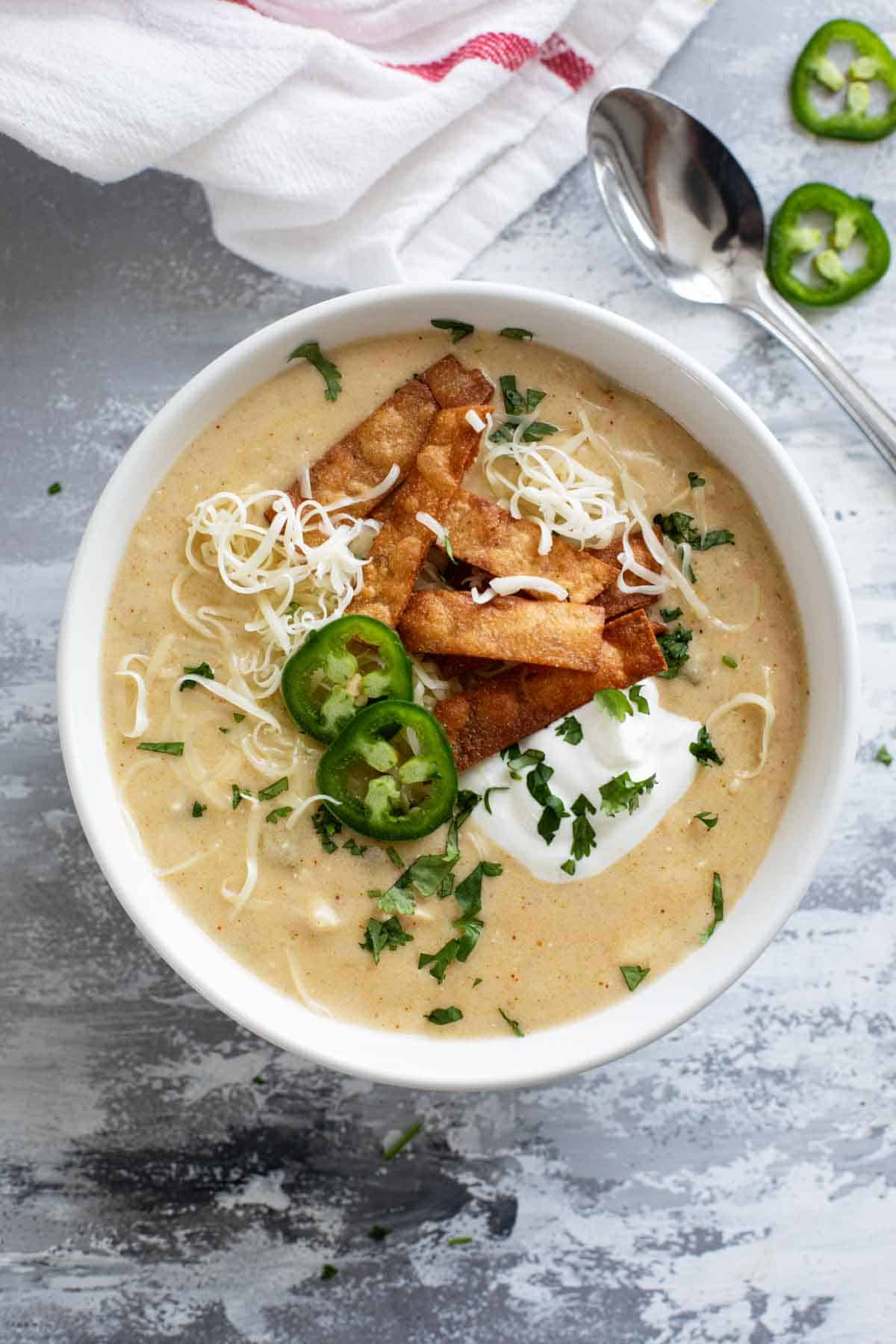 Bowl of green chicken enchilada soup topped with tortilla strips, cilantro, sour cream, and jalapeños.