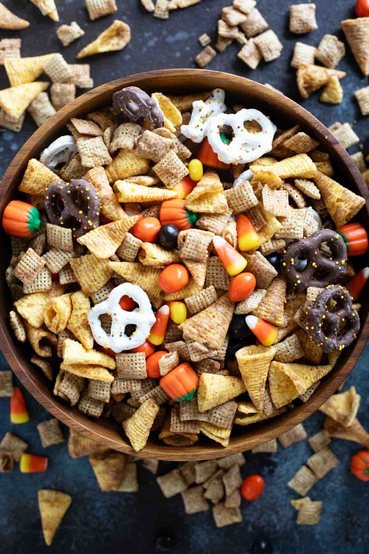 Bowl filled with Halloween Chex mix with some surrounding the bowl.