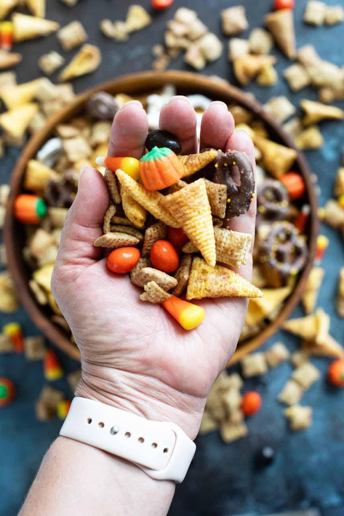 Hand holding Halloween Chex Mix with candy, candy corn, Chex, and bugles.