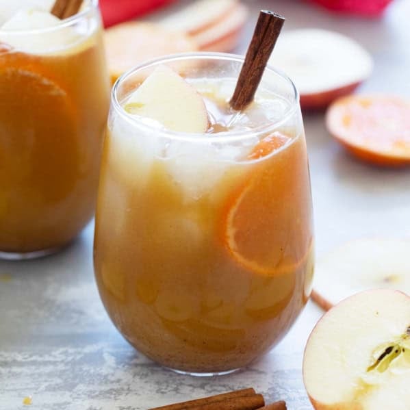 Glass of spiced apple cider punch with a cinnamon stick, apple pieces, and orange slices.