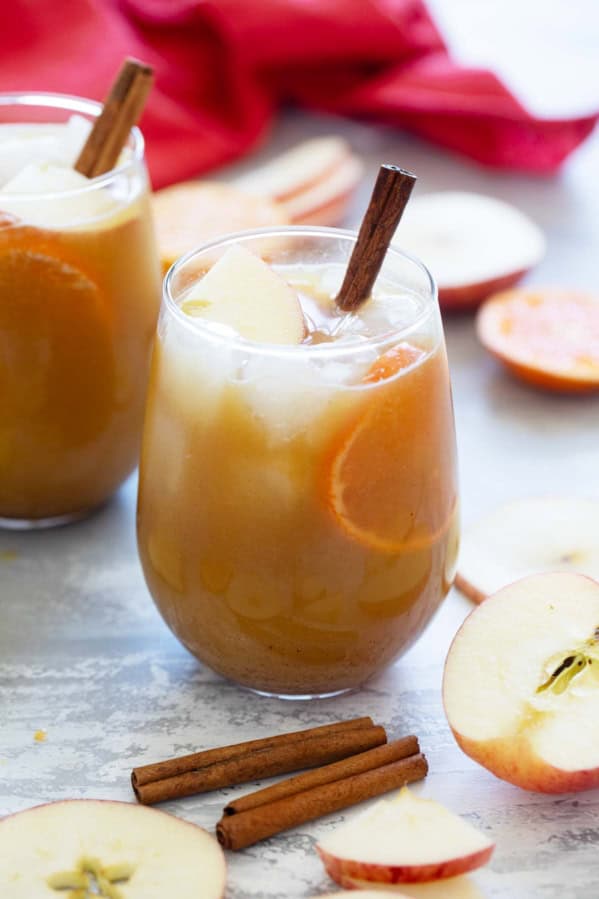 Glass of spiced apple cider punch with a cinnamon stick, apple pieces, and orange slices.